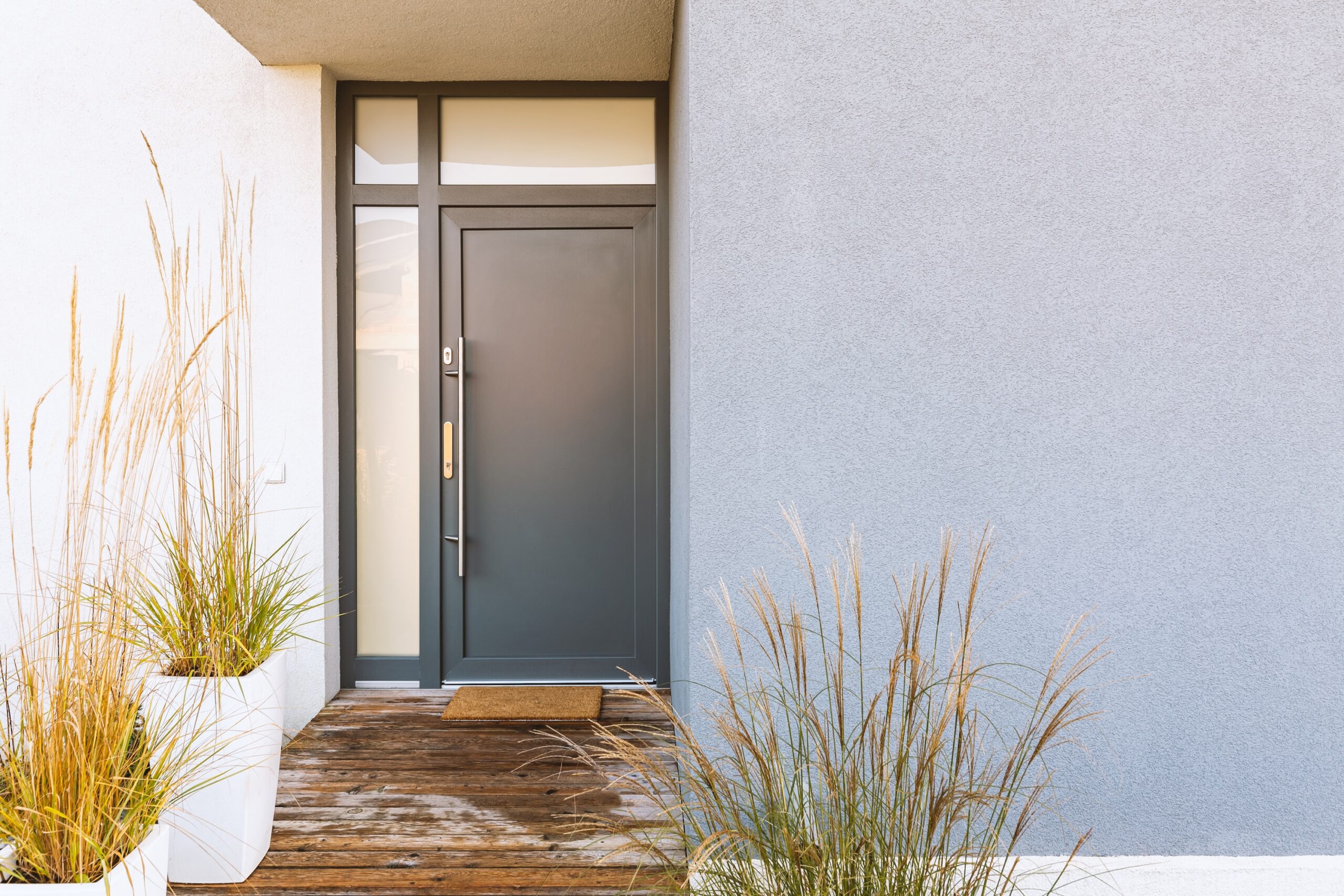 Potted grass and a wooden path in front of the entrance of a stylish suburban house.